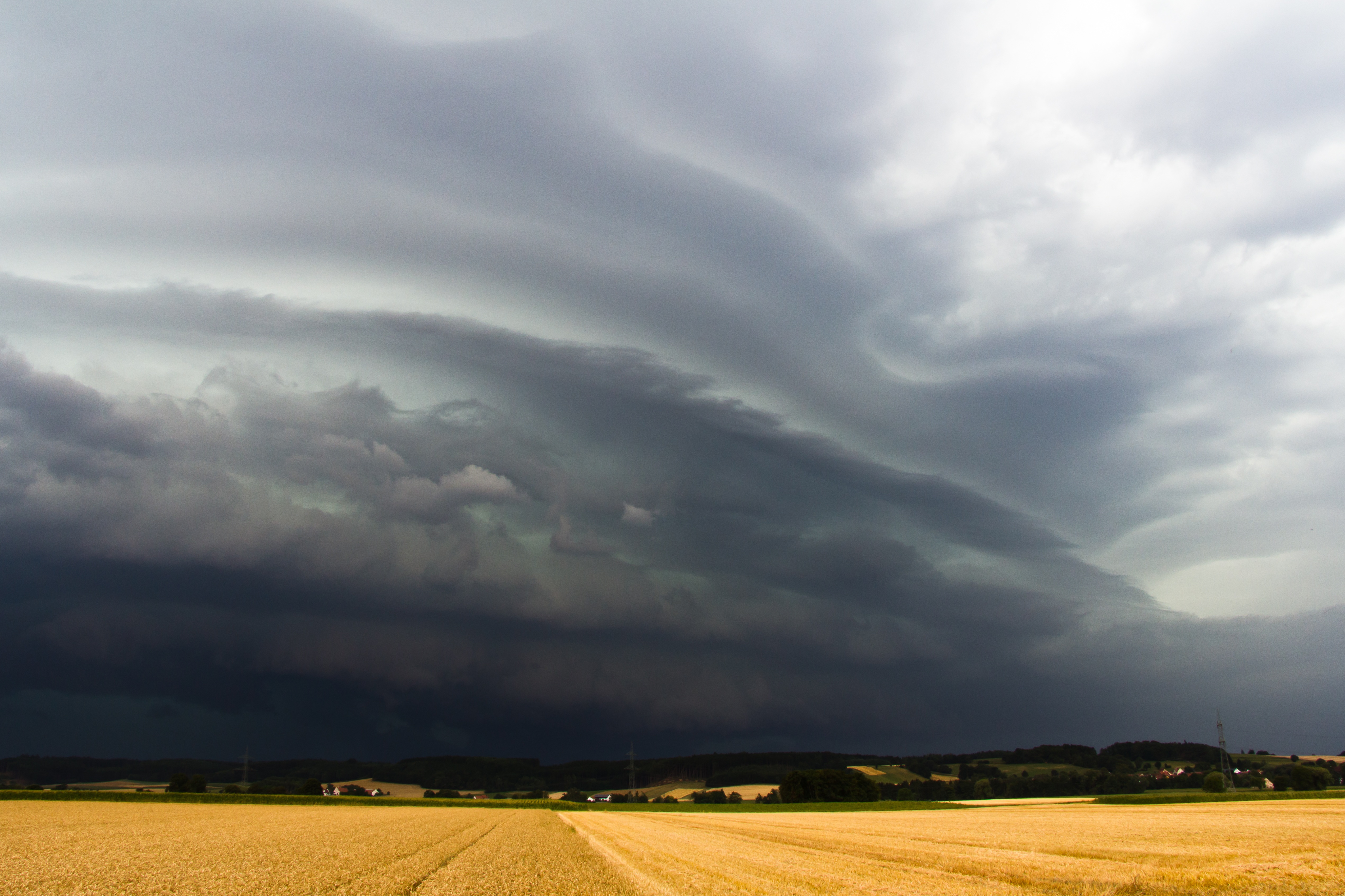 Storm clouds over a wheat field, with wooded hills on the horizon